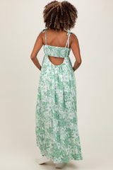 woman wearing a green floral maternity maxi dress with tie straps and an open back, showcasing her baby bump