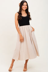 woman wearing a black ribbed tank dress with a beige flowing skirt and pockets, posing with a smile