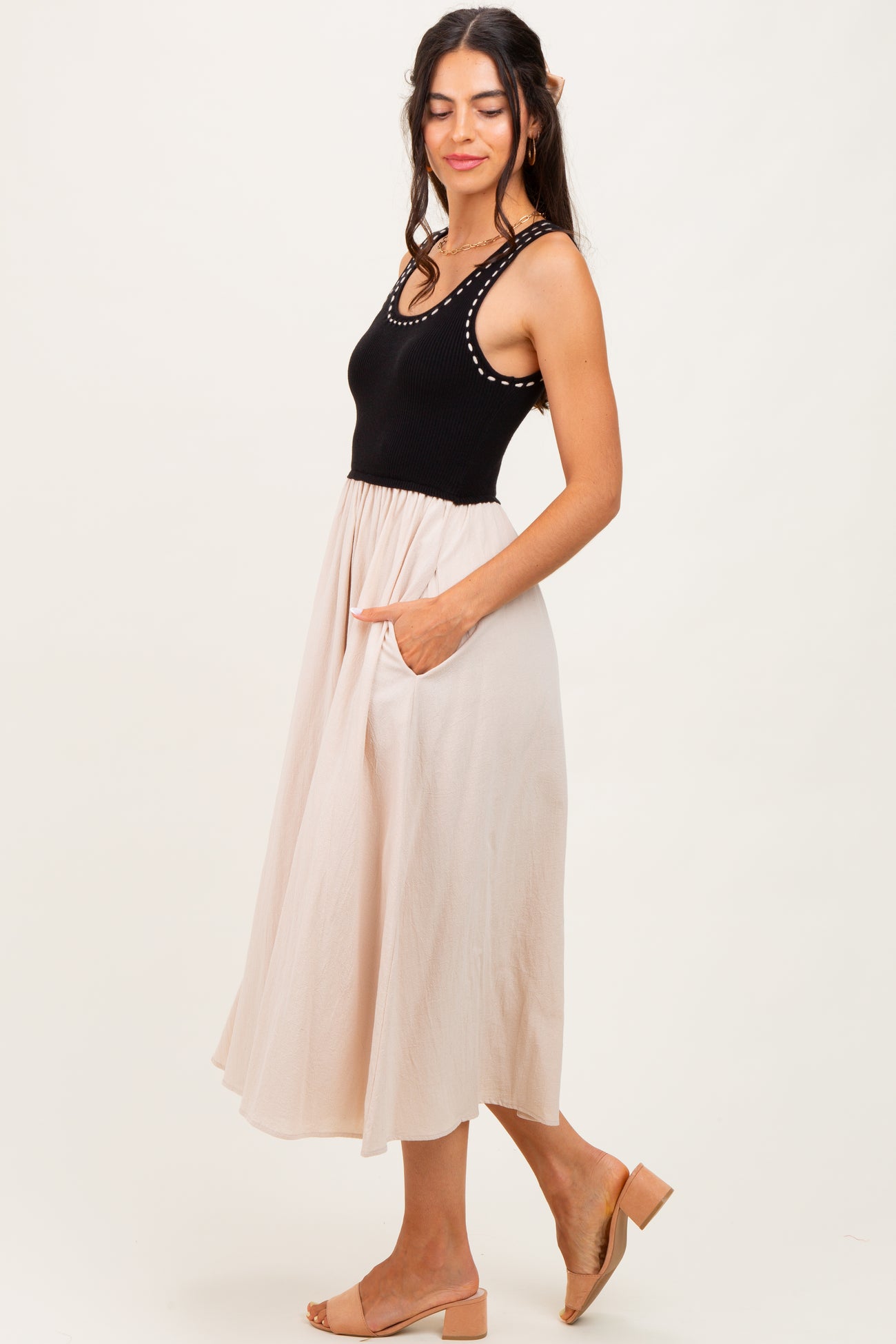 woman wearing a black ribbed tank dress with a beige midi skirt and pockets, standing sideways against a neutral background