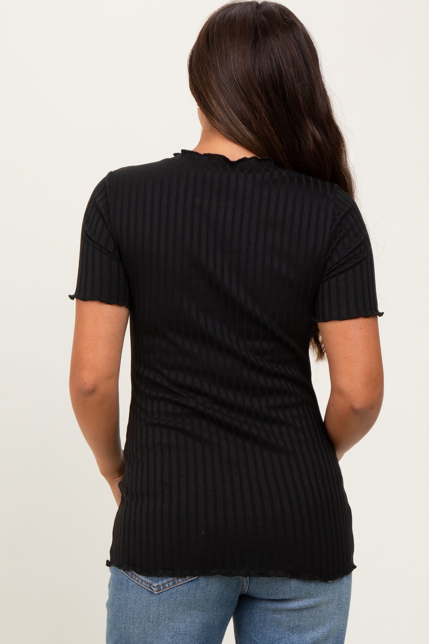 woman wearing a black ribbed short sleeve maternity top, showing the back view, paired with light blue jeans