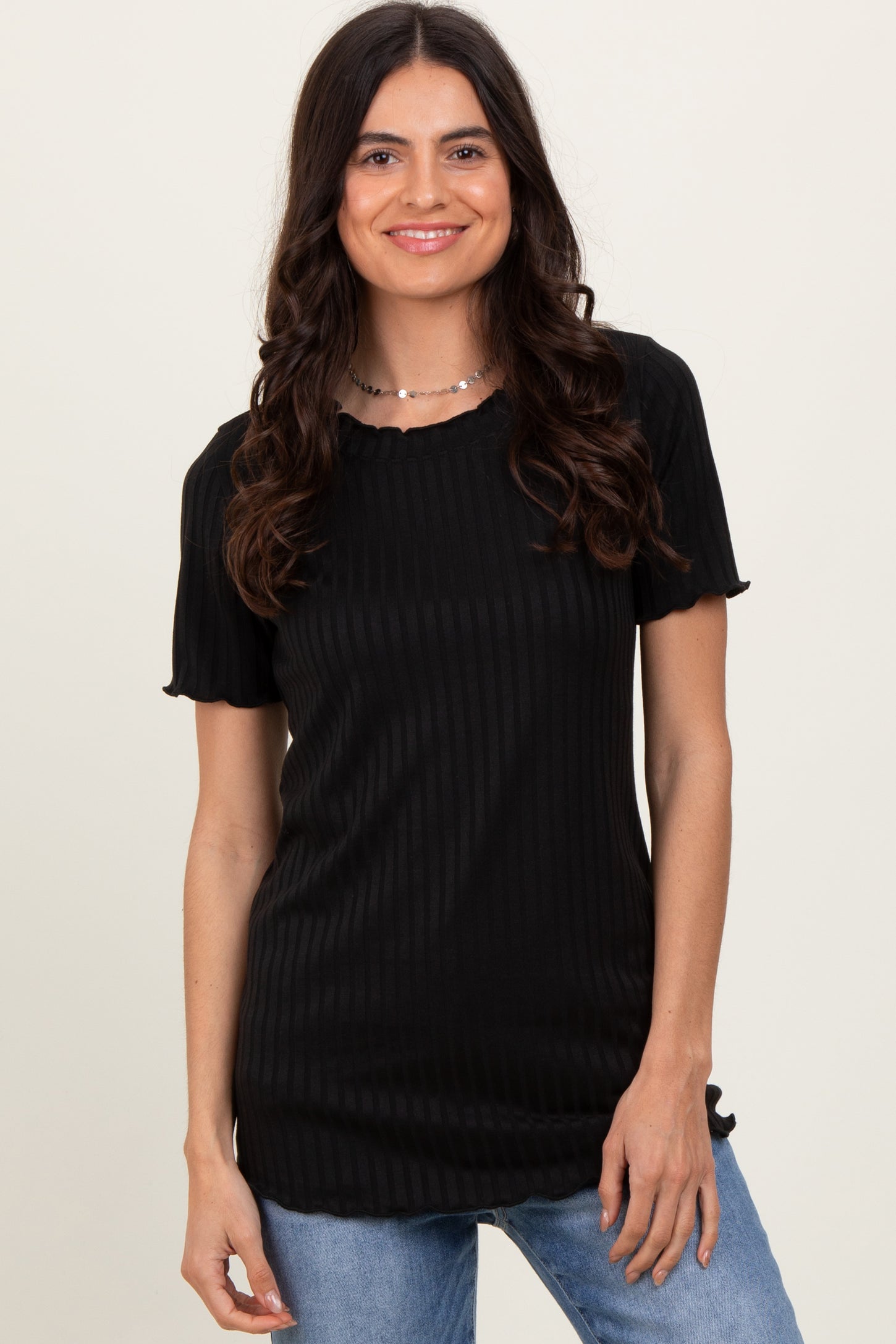 woman wearing a black ribbed short sleeve top with a scalloped neckline and smiling at the camera