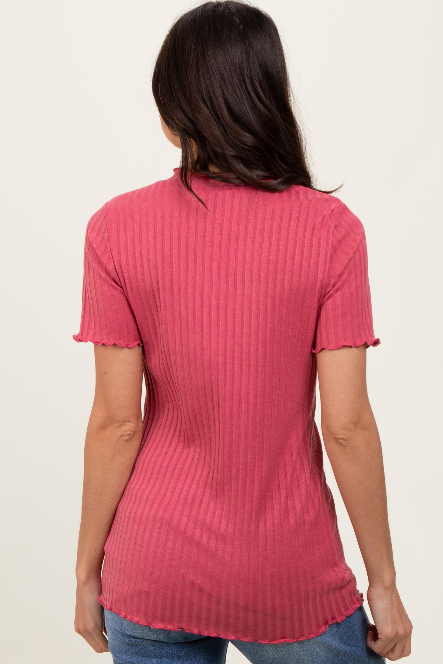 woman wearing a pink ribbed t-shirt with short sleeves and a scalloped hem, seen from the back