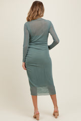 woman wearing a sheer green maternity dress with long sleeves and a fitted silhouette, showcasing a baby bump