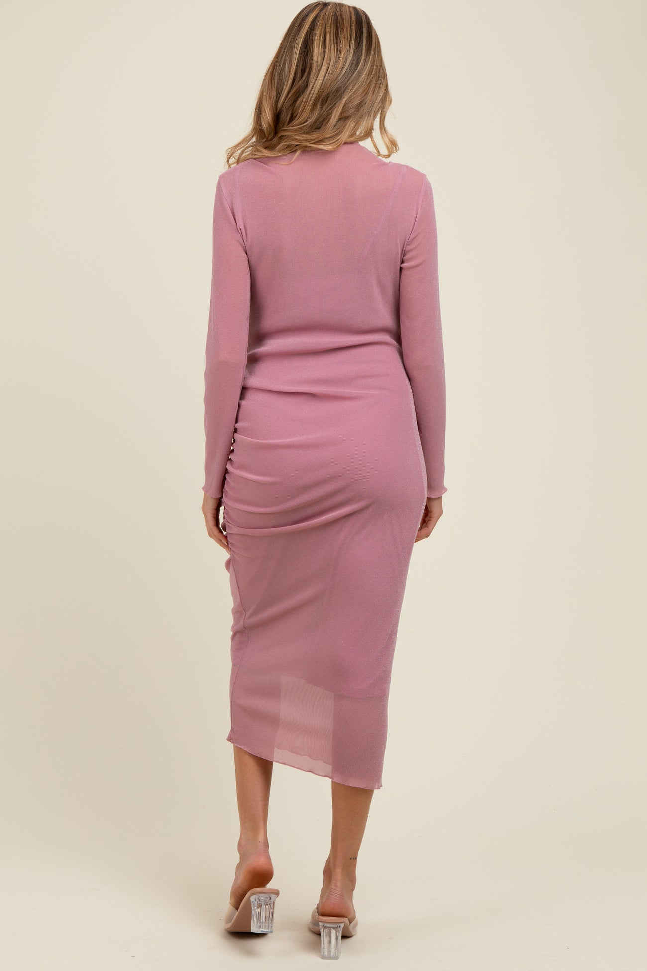 woman wearing a light pink long sleeve maternity dress with ruched detailing at the back and sheer fabric
