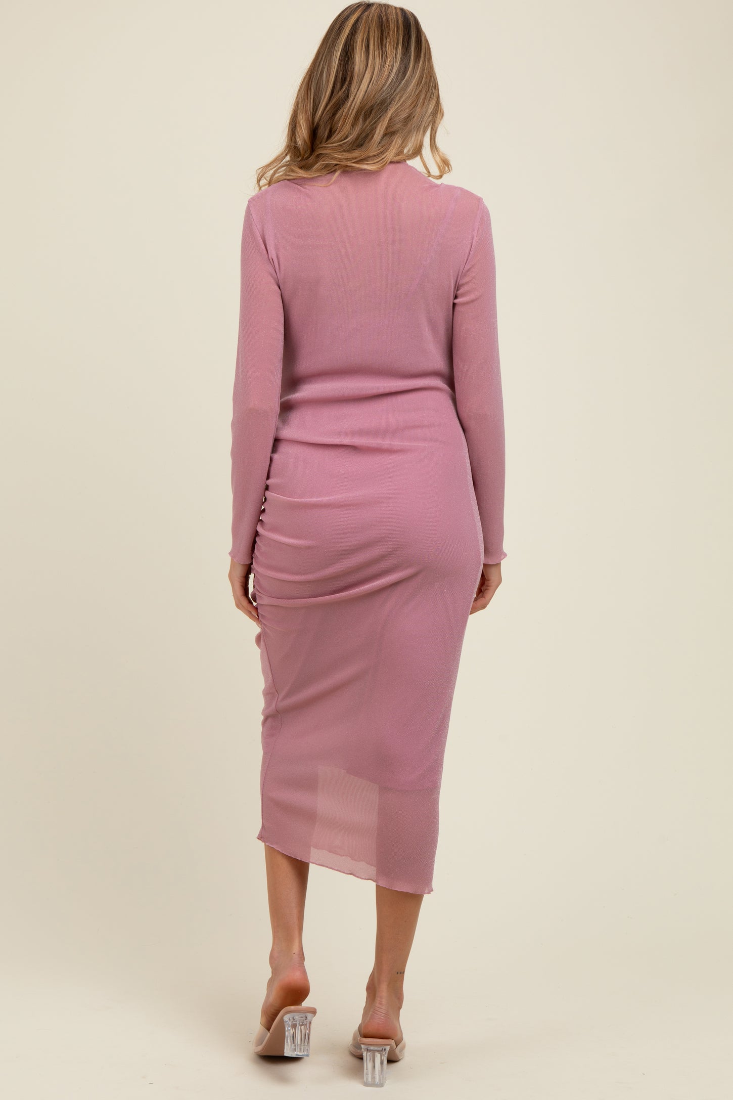 woman wearing a light pink long sleeve maternity dress with ruched detailing at the back and sheer fabric