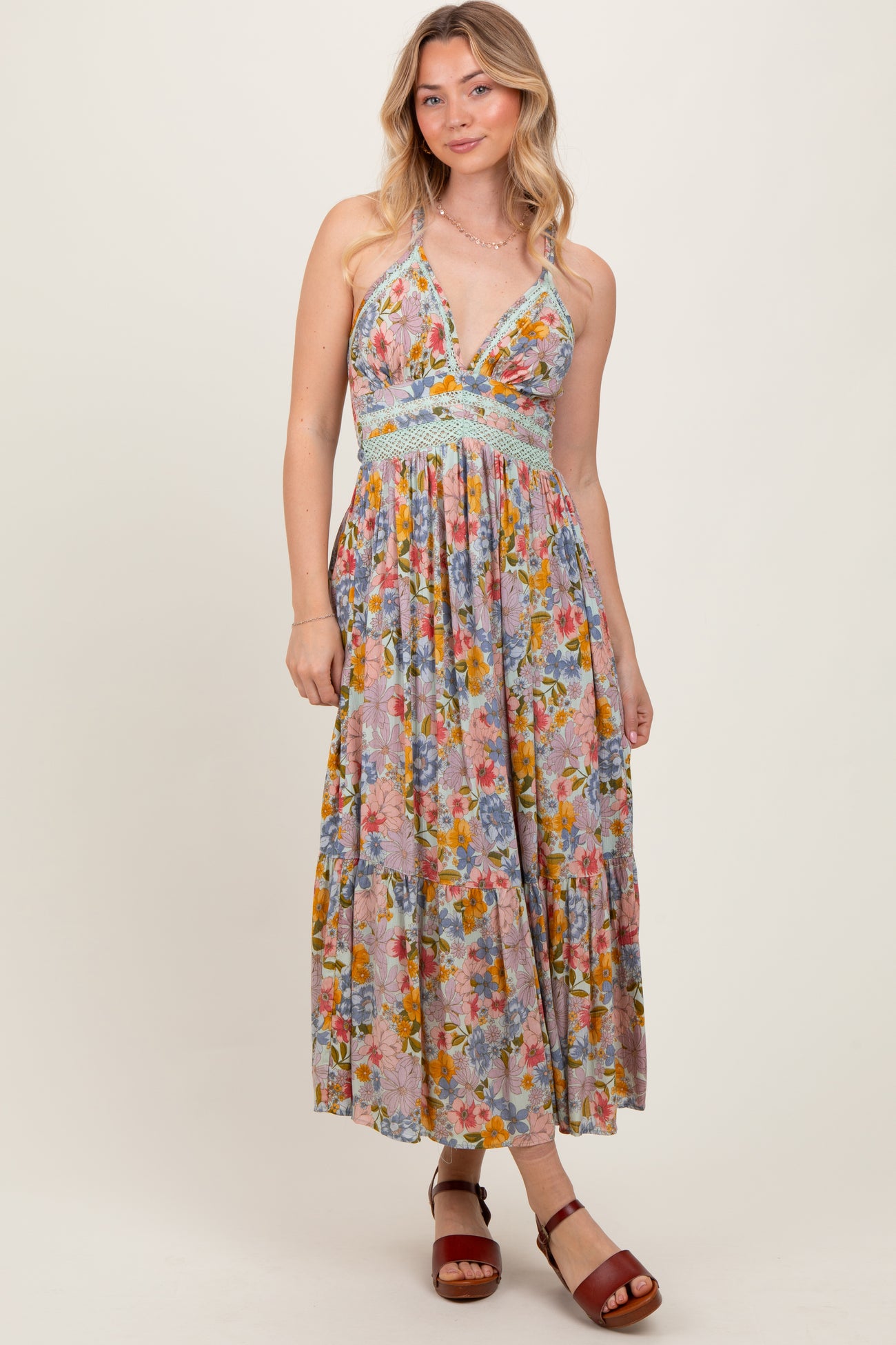 woman wearing a floral maxi dress with a v-neckline and braided details, paired with brown heeled sandals