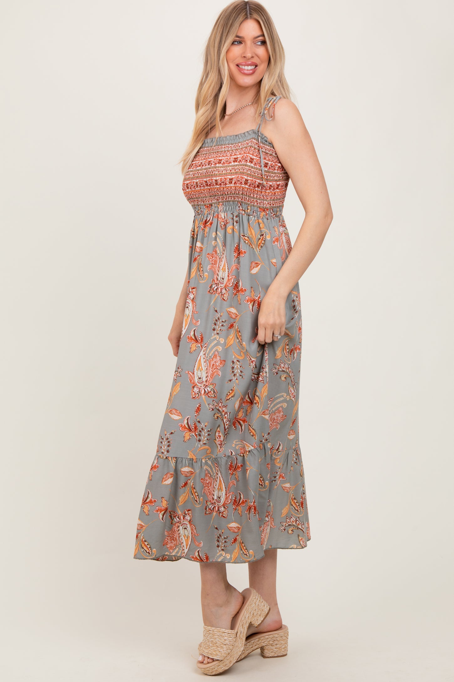 woman wearing a gray floral smocked maxi dress with ruffled hem and strappy details, standing sideways