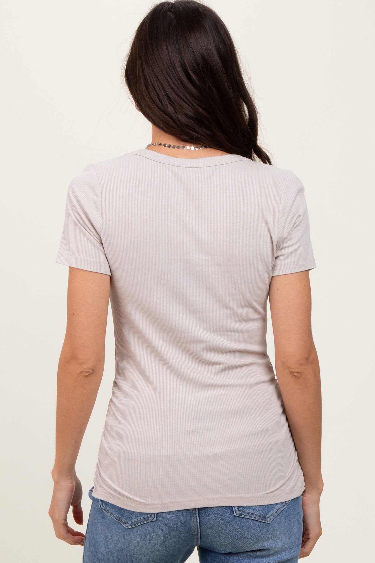 woman wearing a back view of a light beige fitted short sleeve top with a ribbed texture and curved hemline