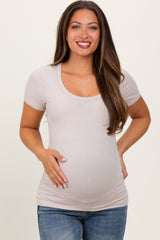 woman wearing a light beige short sleeve maternity top and holding her baby bump