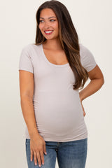 woman wearing a light beige short sleeve maternity top and showing her baby bump with a smile