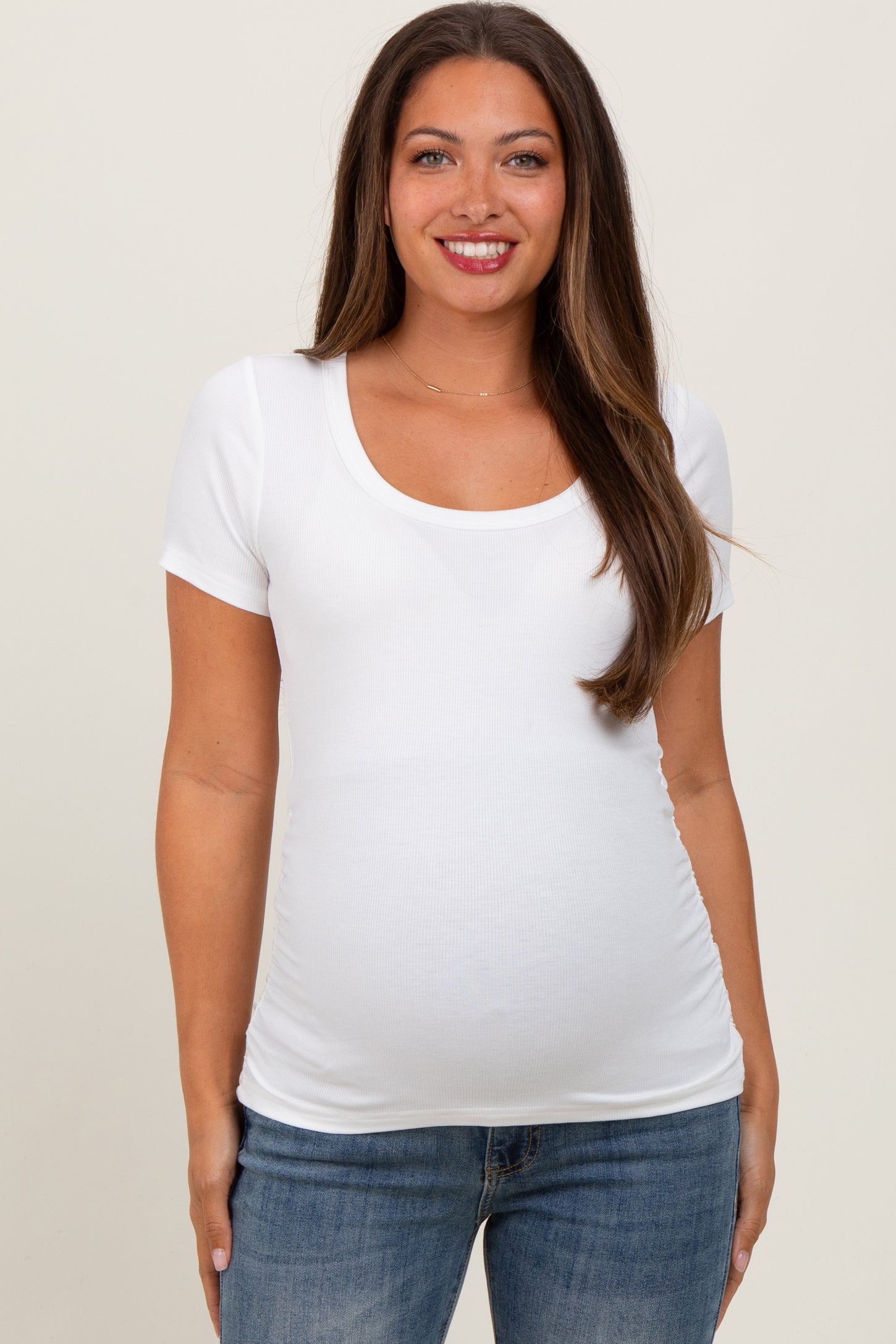 woman wearing a white short sleeve maternity top and showing her baby bump while smiling
