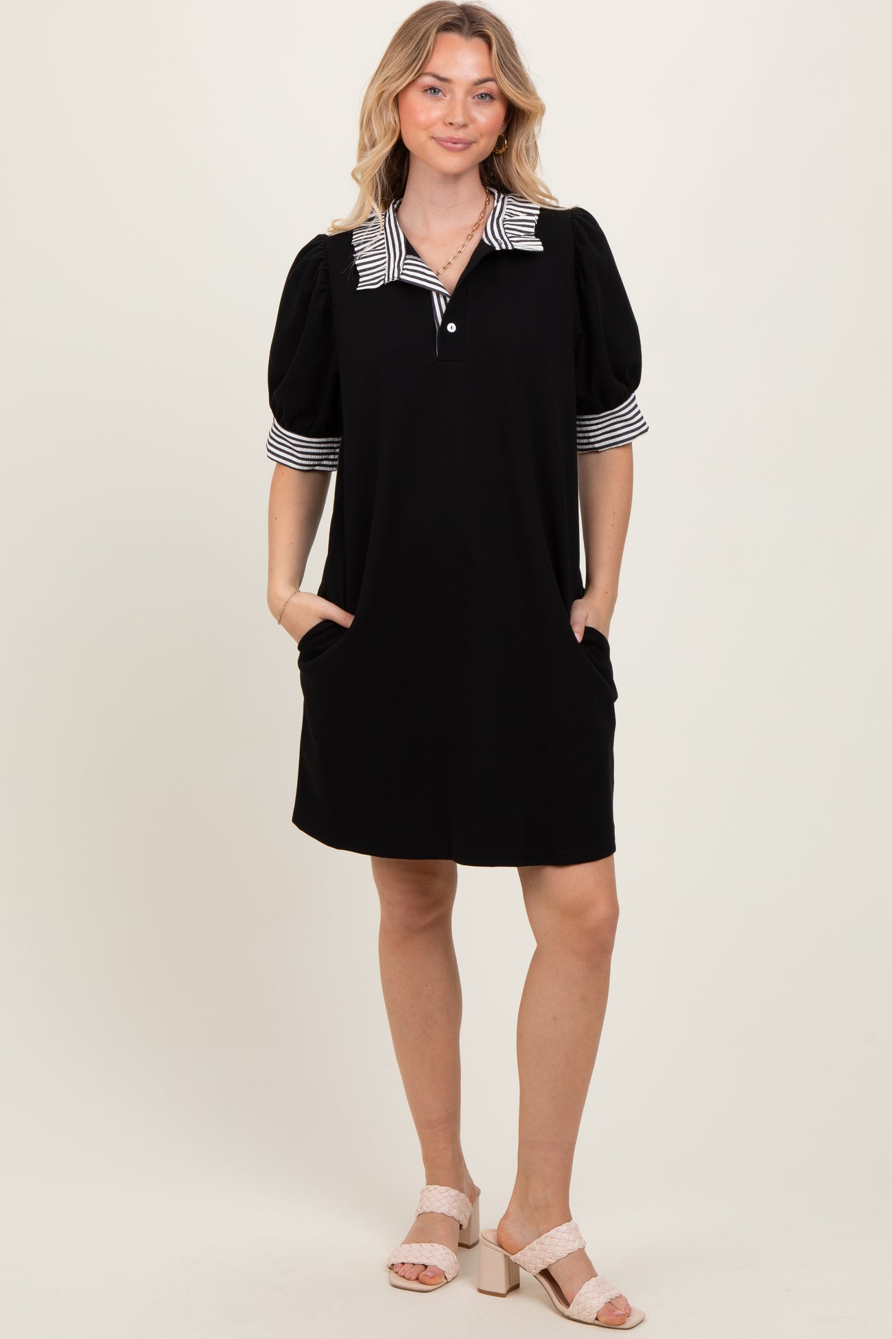 woman wearing a black short sleeve dress with a striped collar and puff sleeves, featuring side pockets