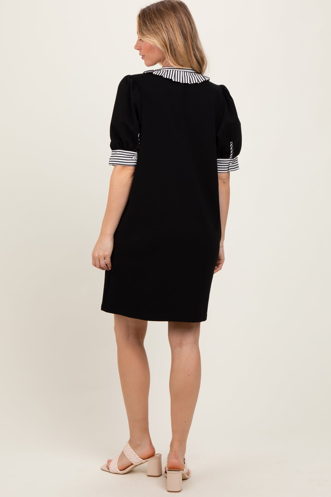 woman wearing a black short sleeve dress with striped cuffs and a collar, standing with her back to the camera