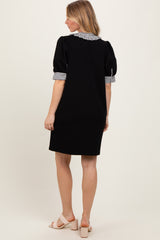 woman wearing a black short sleeve dress with striped cuffs and a collar, standing with her back to the camera