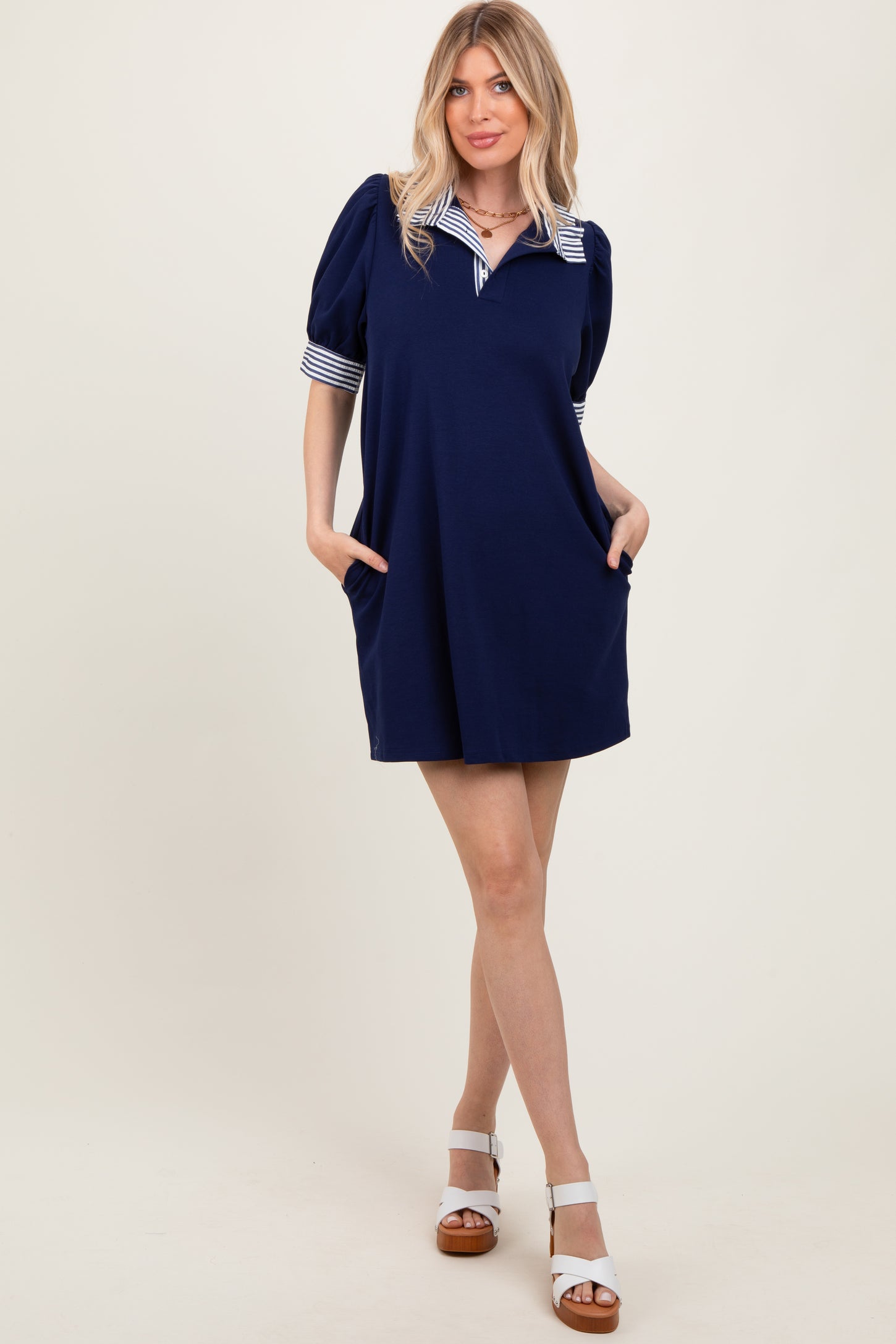 woman wearing a navy short sleeve dress with striped collar and puff sleeves, standing with hands in pockets