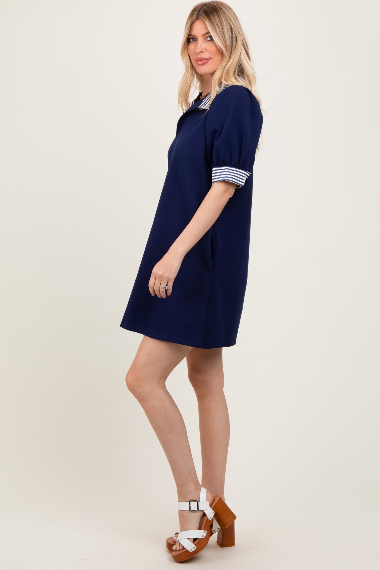 woman wearing a navy blue short sleeve dress with striped collar and cuffs, standing sideways