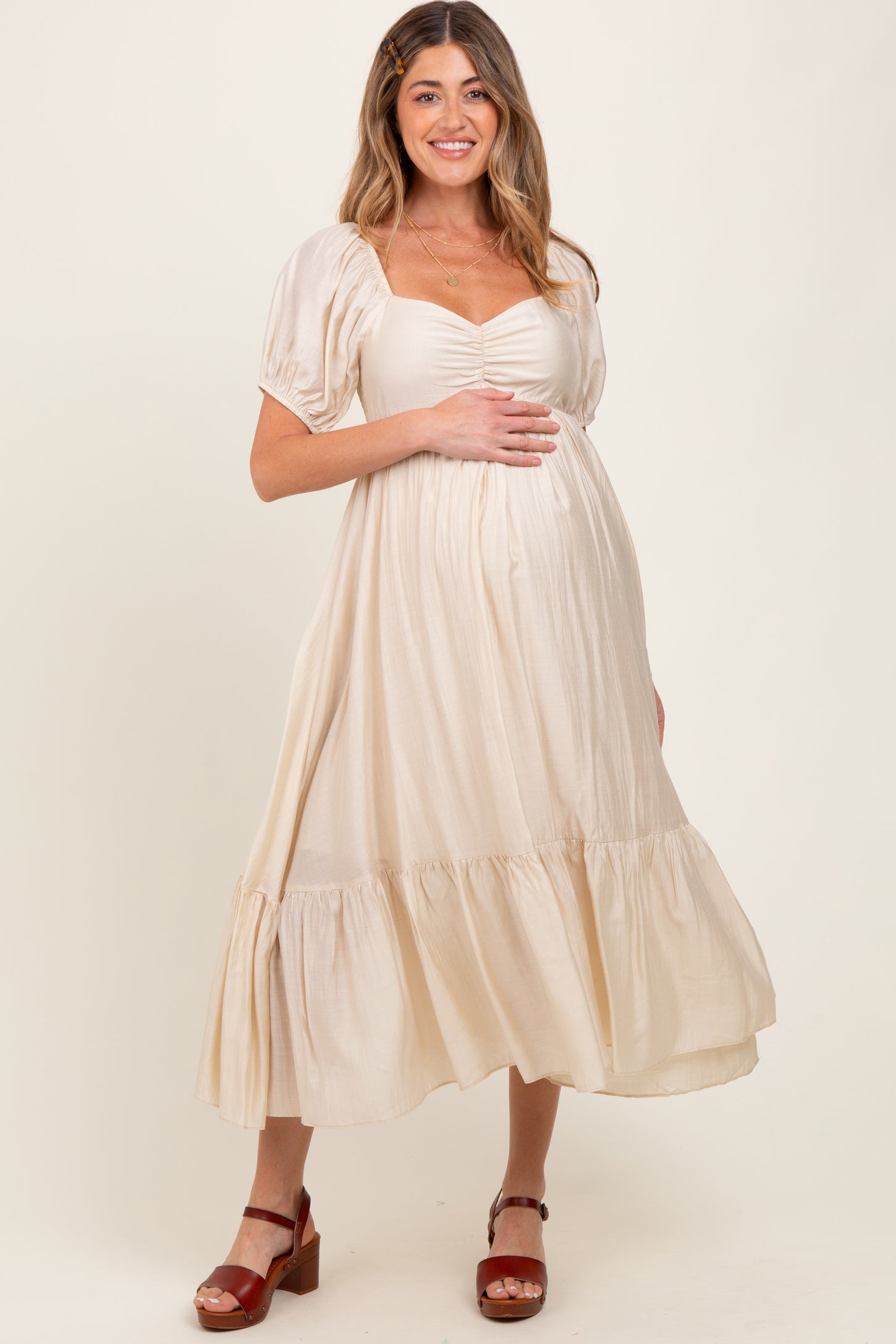 woman wearing a cream maternity dress with puff sleeves and a tiered skirt, holding her baby bump
