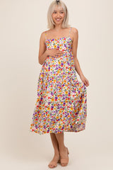 woman wearing a floral maternity dress with adjustable straps and a baby bump, standing and smiling