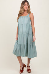 woman wearing a flowy teal maternity dress with tiered details and buttons, showcasing her baby bump