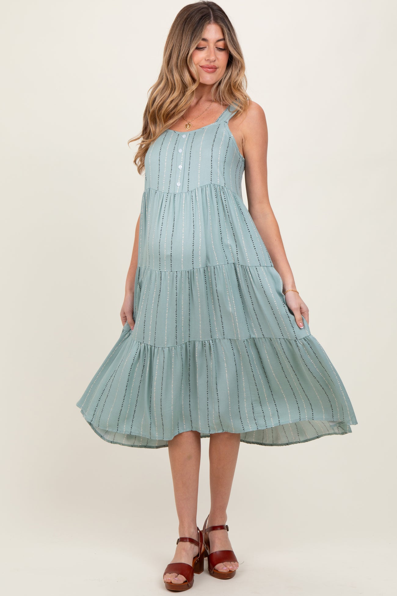 woman wearing a light teal maternity dress with tiered design and buttons, showing a baby bump