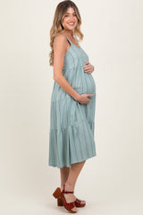 woman wearing a mint green tiered maternity dress, gently cradling her baby bump while smiling