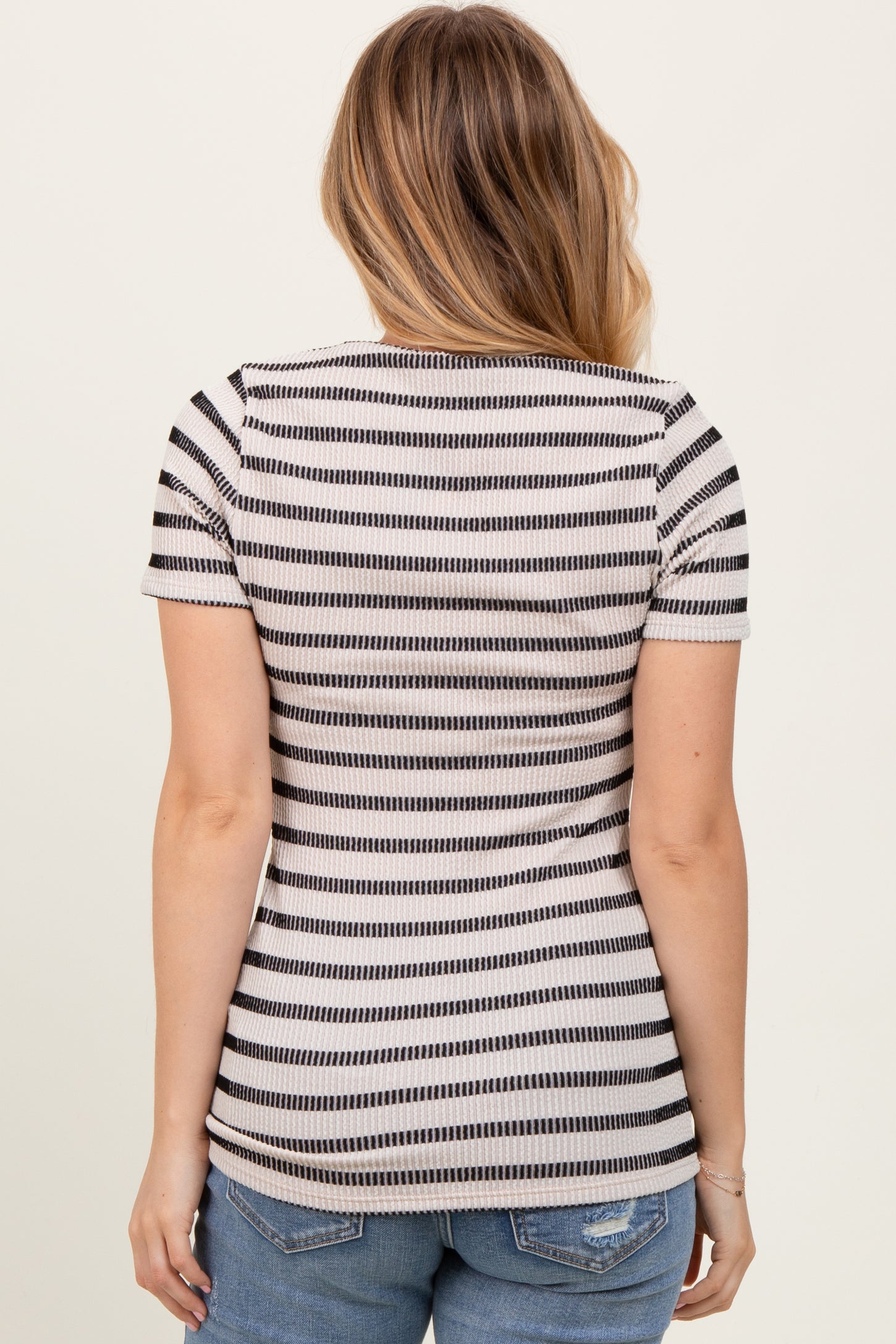 woman wearing a black and cream striped short sleeve top, seen from the back, paired with denim shorts