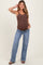 woman wearing a brown ribbed maternity tank top and blue flared jeans, posing with one hand on her hip and showcasing her baby bump