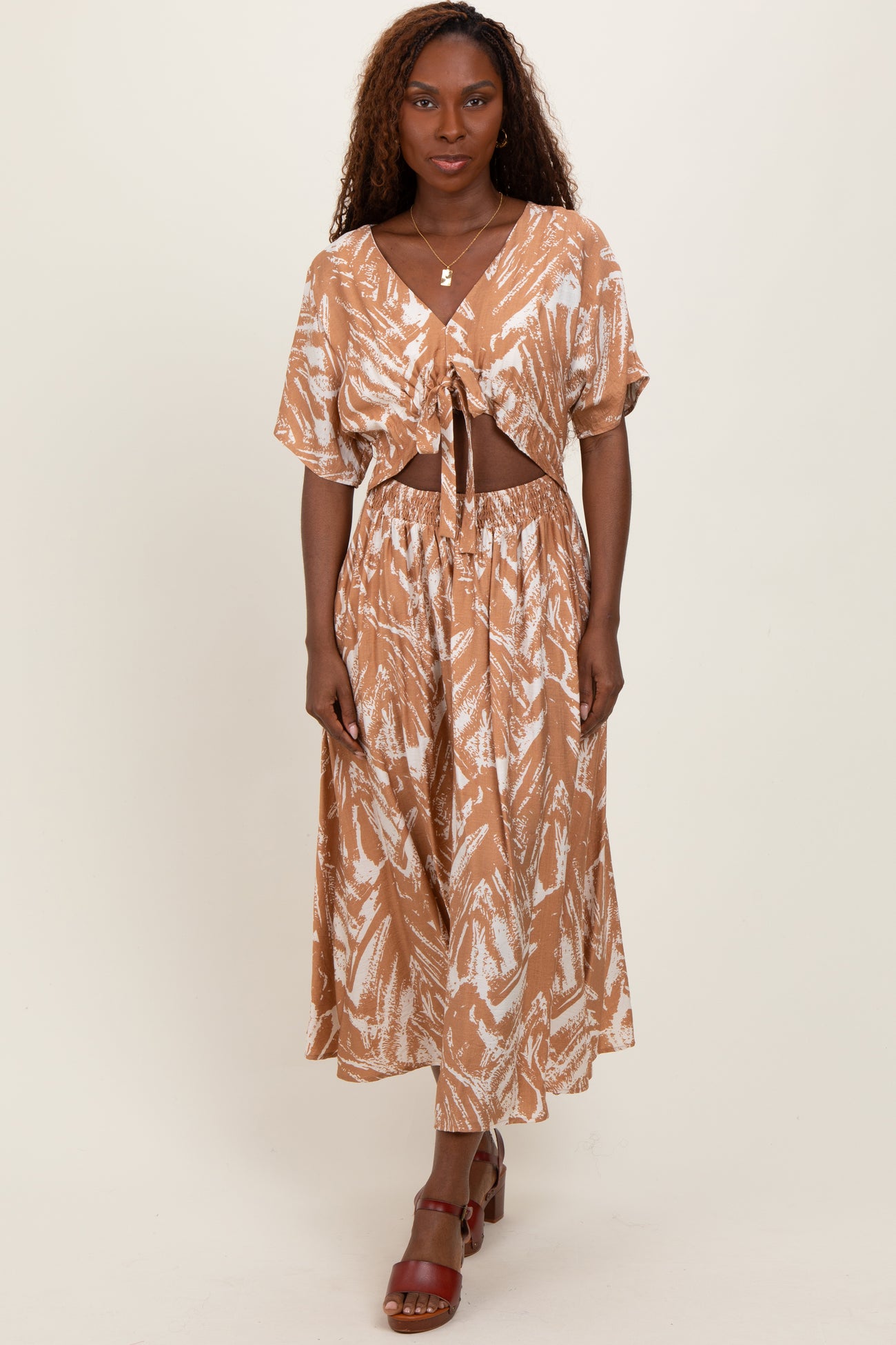 woman wearing a brown tie-front cropped top and matching maxi skirt with a leaf print and high slit