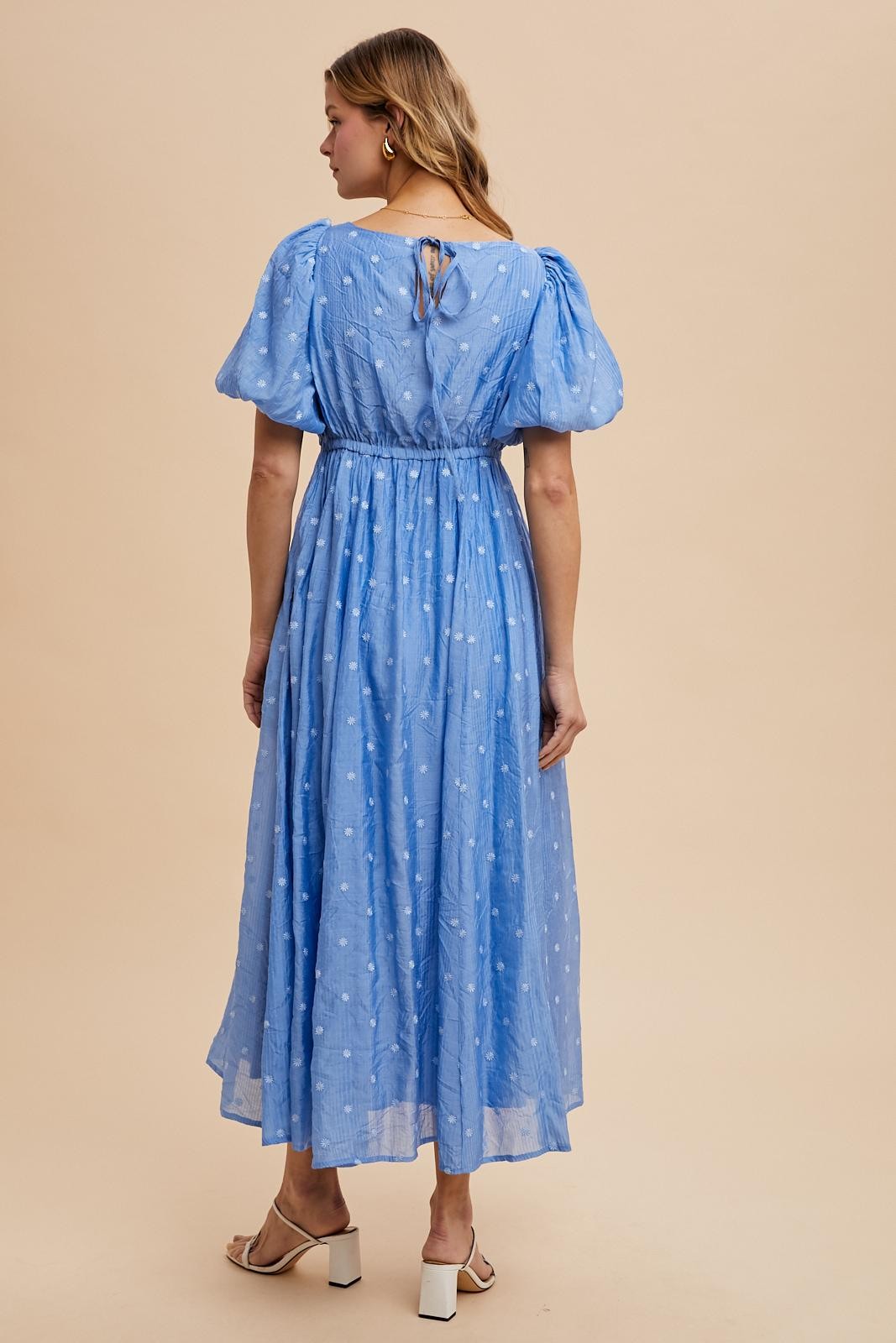 woman wearing a light blue puff sleeve maxi dress with a cinched waist and white polka dots, showing the back detail