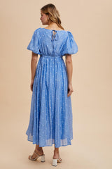 woman wearing a light blue puff sleeve maxi dress with a cinched waist and white polka dots, showing the back detail