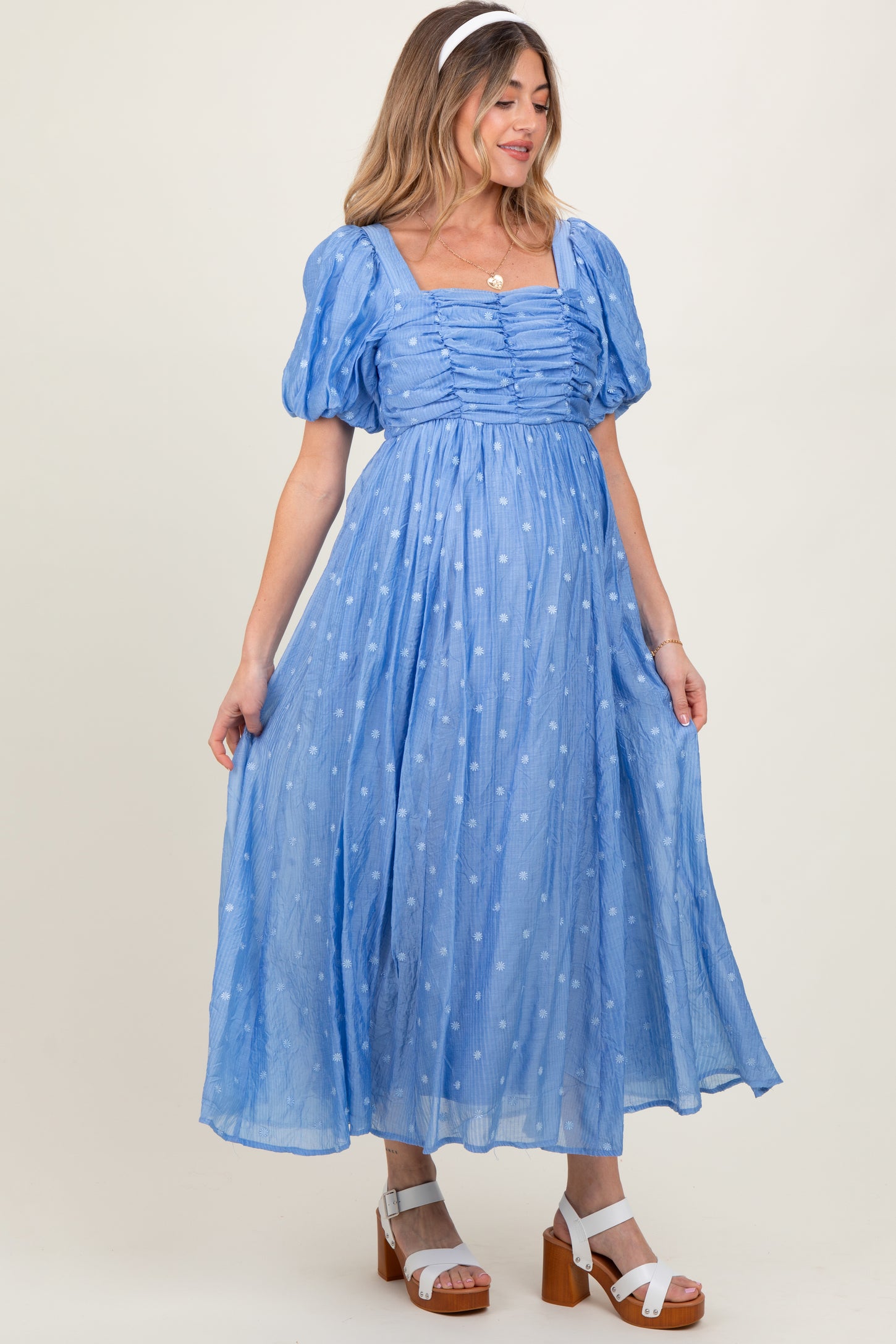 woman wearing a light blue maternity dress with puff sleeves and polka dot details, showing her baby bump