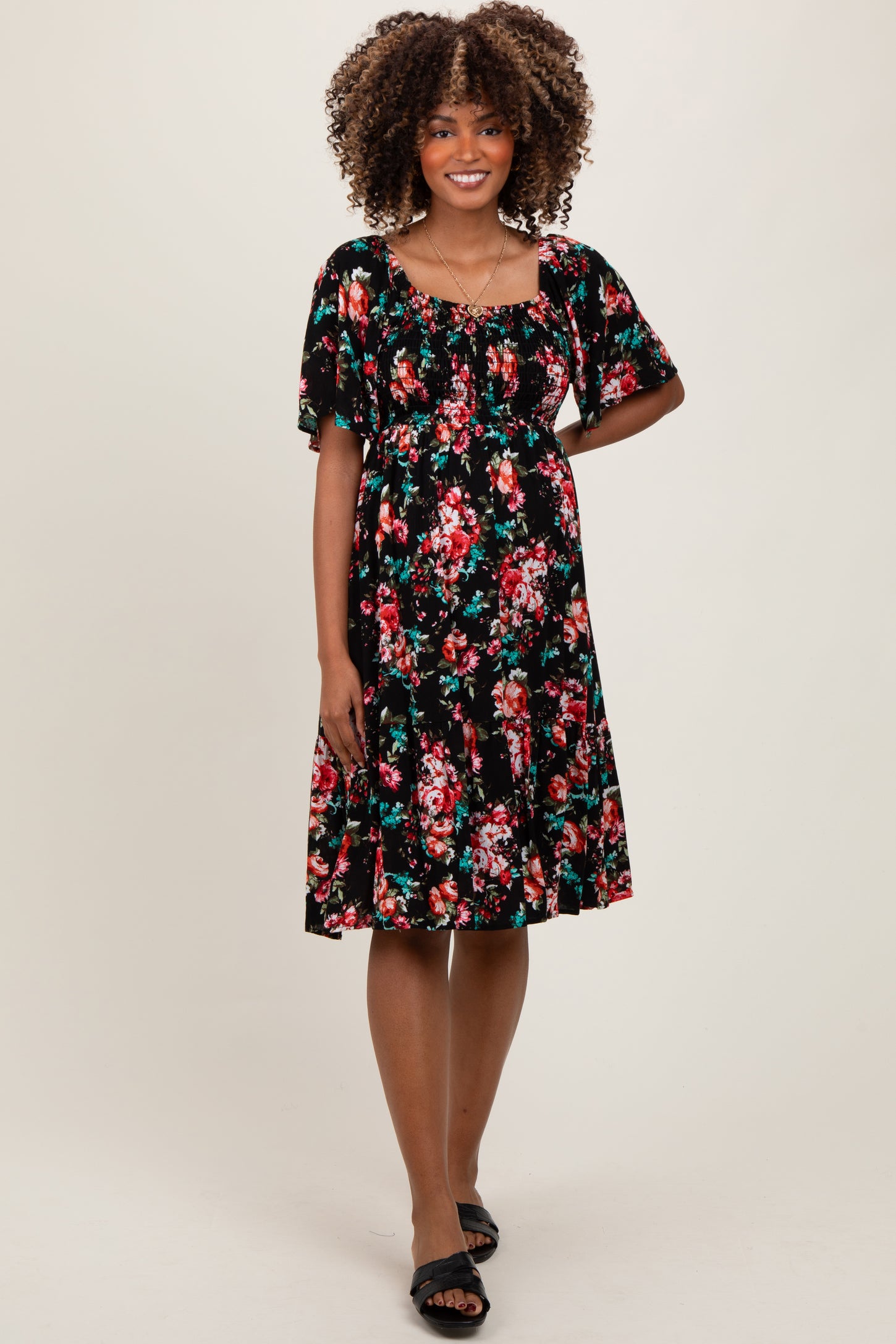 woman wearing a black floral maternity dress with short sleeves and a fitted bodice, showing her baby bump