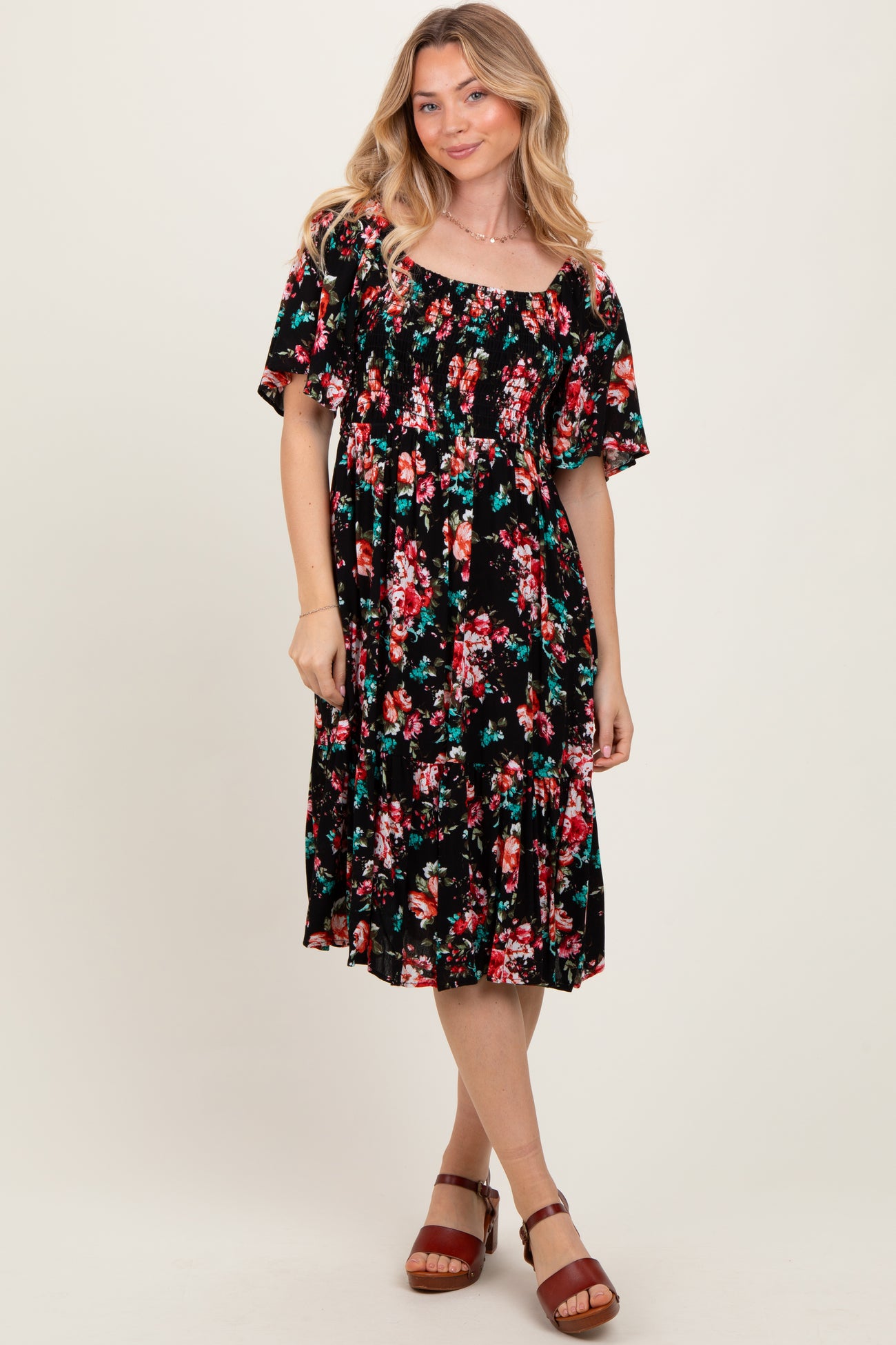 woman wearing a black floral midi dress with short sleeves and a gathered waist, standing and smiling