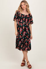 woman wearing a black floral midi dress with short sleeves and a gathered waist, standing and smiling