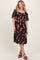 woman wearing a black floral midi dress with short sleeves and a gathered waist, standing and smiling