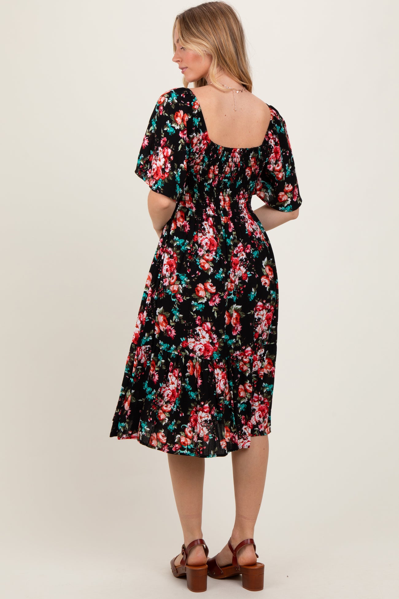 woman wearing a black floral smock dress with short sleeves and a tiered hem, viewed from the back