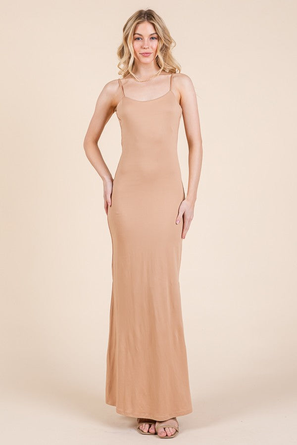 woman wearing a nude sleeveless maxi dress with a fitted silhouette and a scoop neckline