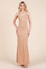 woman wearing a nude sleeveless maxi dress with a fitted silhouette and a scoop neckline