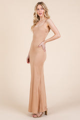 woman wearing a nude spaghetti strap maxi dress with a fitted silhouette and side slit