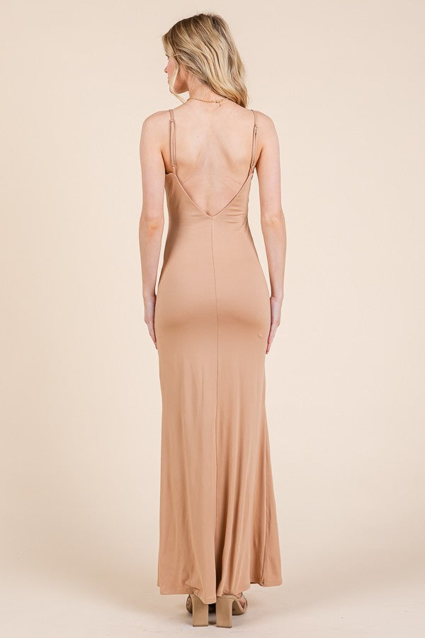 woman wearing a fitted nude maxi dress with a deep V-back and thin straps, showing a sleek silhouette from the back