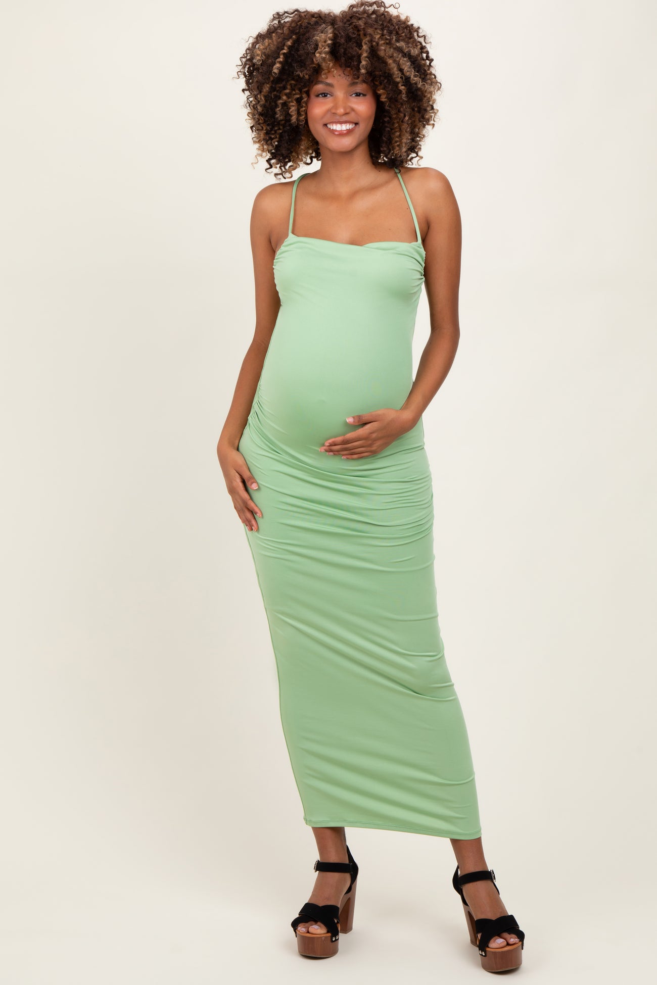 woman wearing a light green maternity maxi dress and holding her baby bump