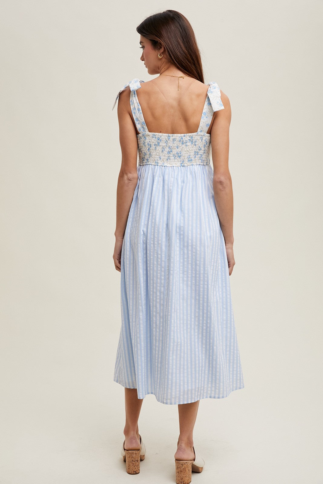 woman wearing a light blue striped midi dress with floral details and tie straps, shown from the back