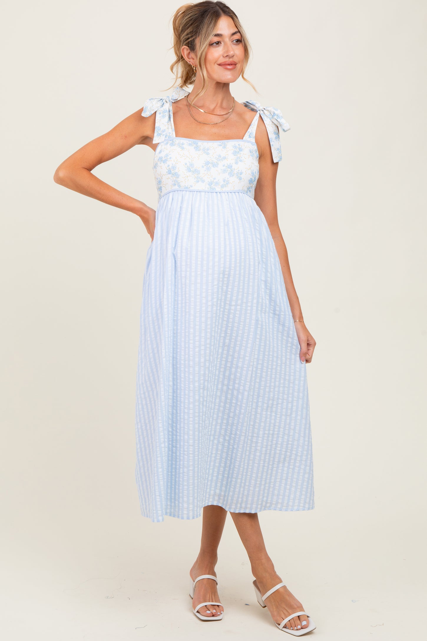 woman wearing a light blue maternity dress with floral print and tie straps, showing her baby bump