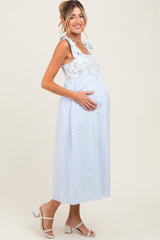 woman wearing a light blue and white striped maternity dress with tie straps and cradling her baby bump