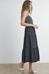 woman wearing a black and white striped tank top with a long black tiered maxi skirt and flat sandals