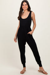 woman wearing a black sleeveless jumpsuit with pockets and tapered legs, styled with flat sandals