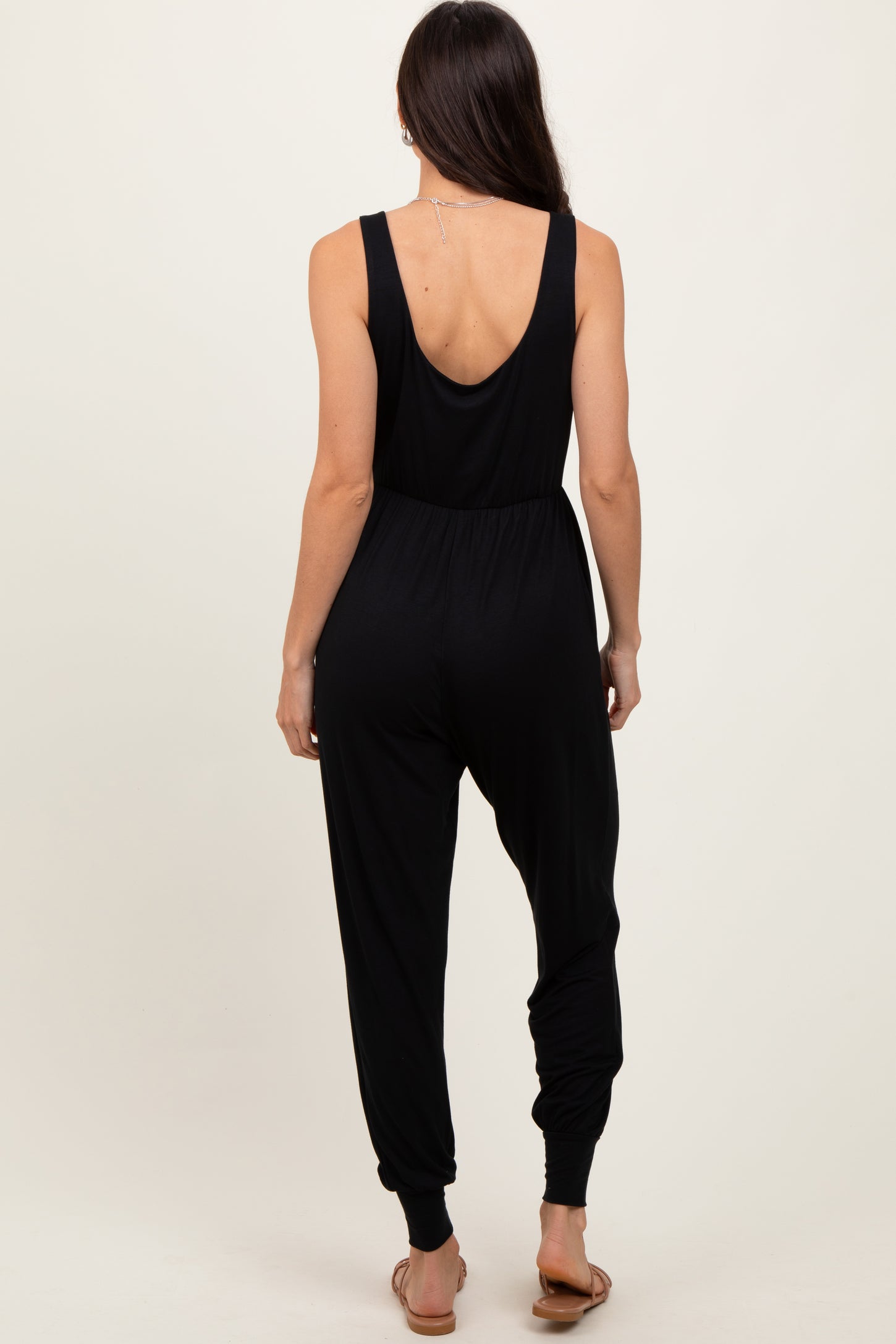 woman wearing a black sleeveless jumpsuit with a low back and tapered ankles, seen from the back