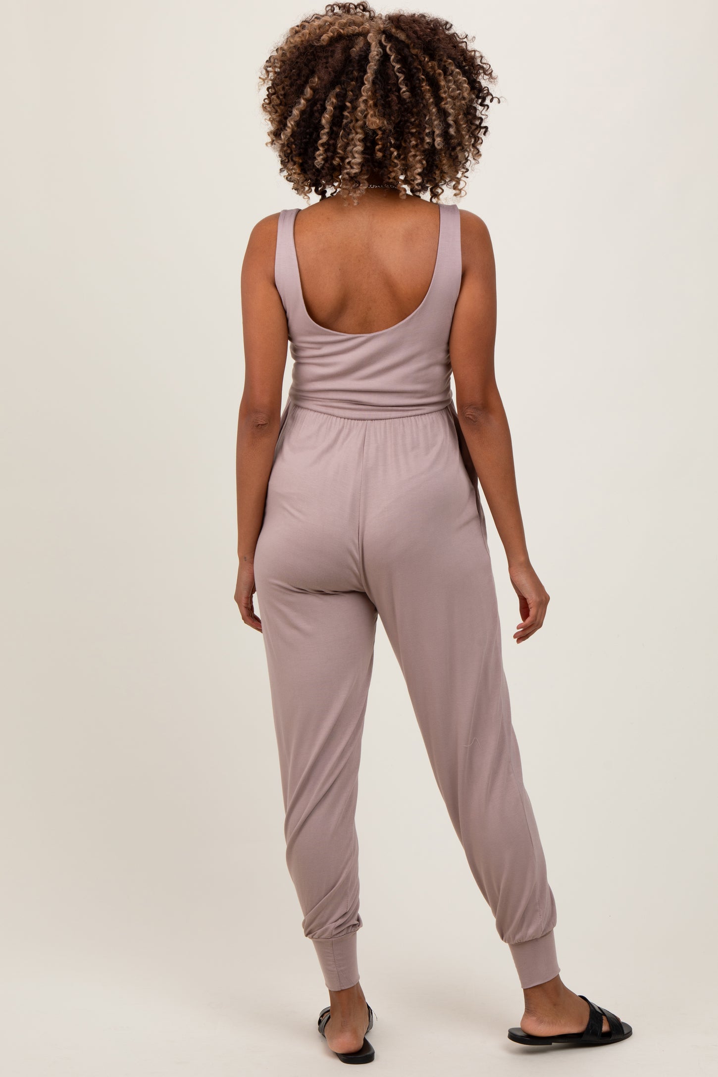 woman wearing a light mauve maternity jumpsuit with a fitted waist and tapered legs, viewed from the back
