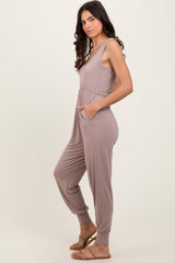 woman wearing a taupe sleeveless jumpsuit with pockets and fitted cuffs, standing sideways