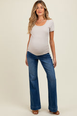woman wearing a beige scoop neck maternity top and blue flared maternity jeans with a visible baby bump
